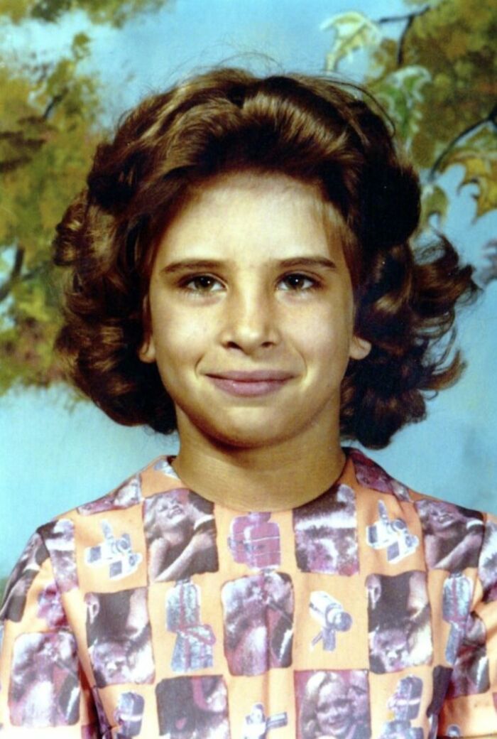 Young girl with distinctive vintage hairstyle wearing a colorful patterned dress during a funny school picture day fail.