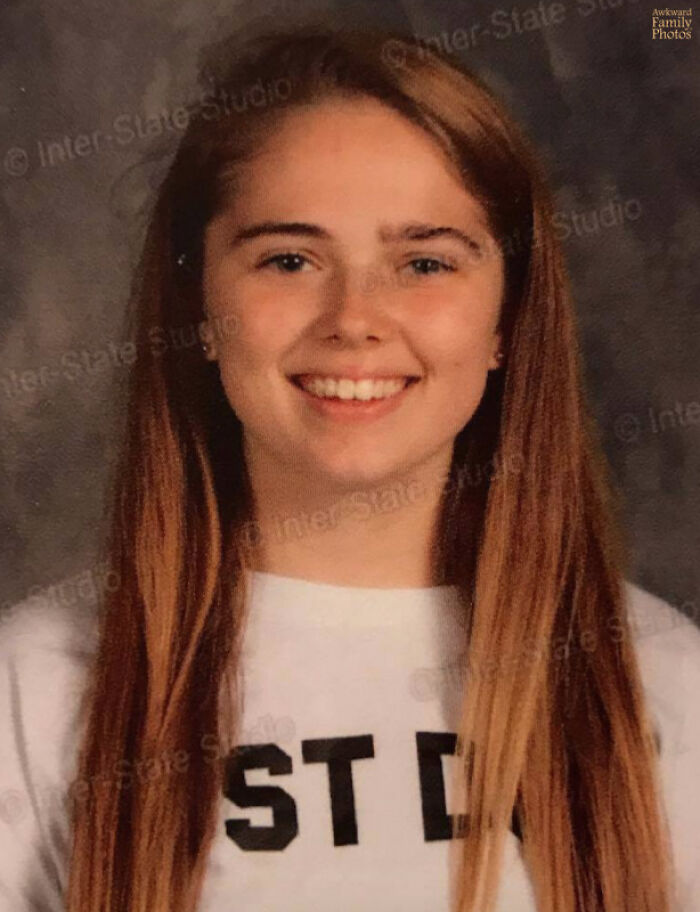 Smiling teenage girl with uneven eyebrows in a funny school picture day fail portrait with long hair and a white shirt.