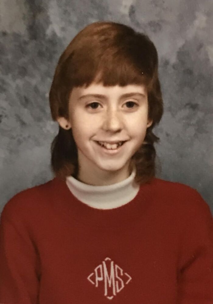 Young student smiling awkwardly in red sweater during a funny school picture day fail with retro hairstyle and earrings.