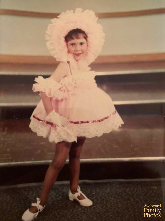 Child in a frilly pink dress and bonnet posing awkwardly for a funny school picture day fail.