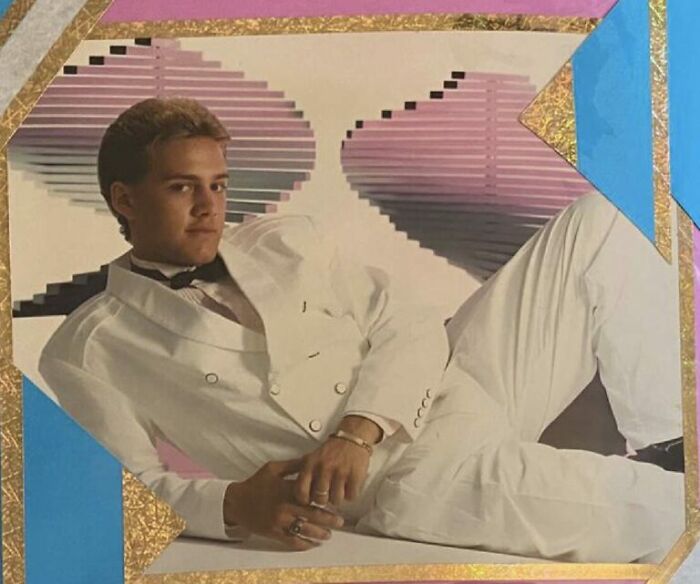 Teen boy in white tuxedo posing awkwardly for a funny school picture day fail with a colorful 90s-style background.