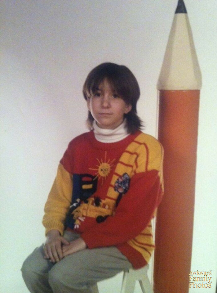School picture day fail with a kid wearing a colorful sweater sitting next to a giant pencil prop in a studio setting.