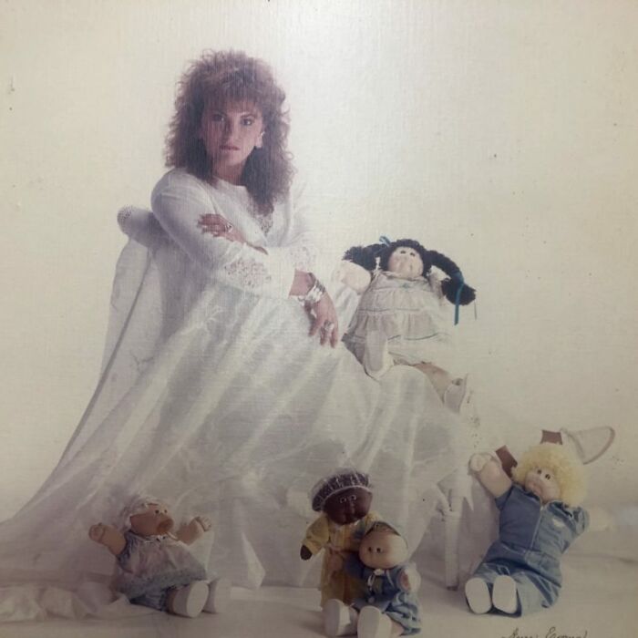 Woman in a vintage white dress posing with dolls in a retro setting, capturing funny school picture day fails vibes