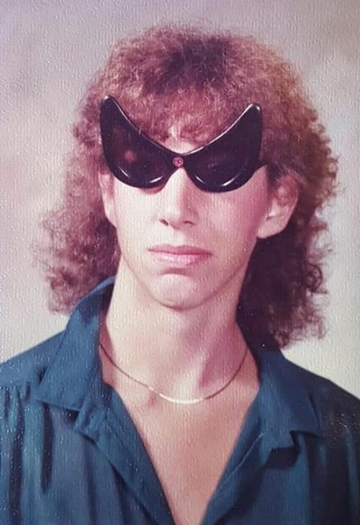 Teen with curly hair wearing oversized cat-eye sunglasses in a vintage funny school picture day fails portrait.