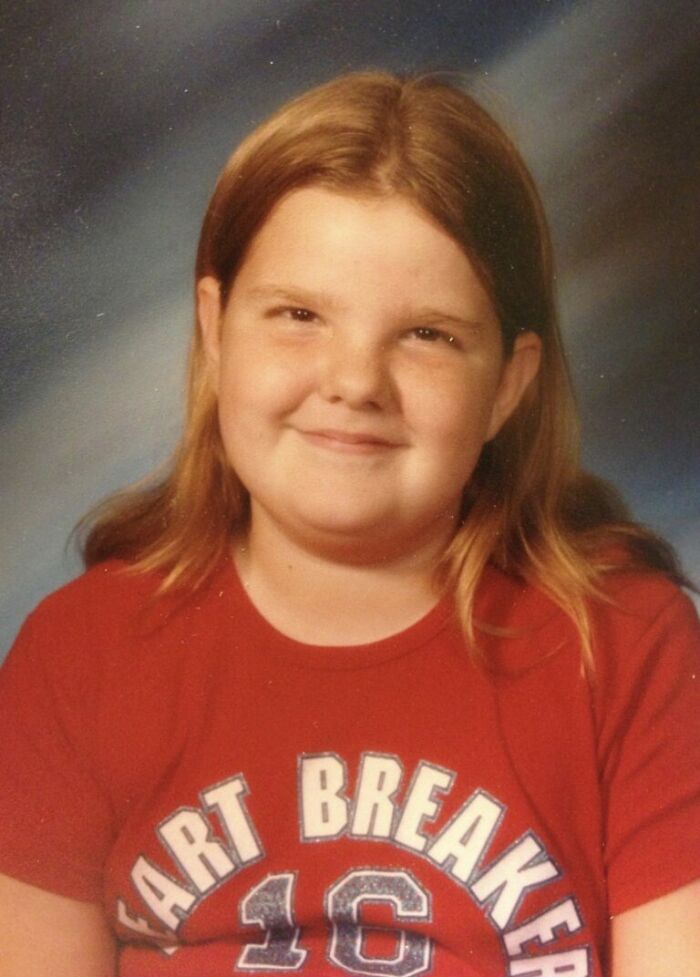 Smiling kid with long hair wearing a red shirt posing for a funny school picture day fails portrait.