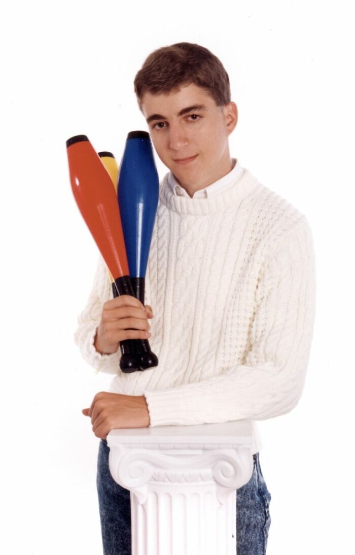 Teen boy in a white sweater posing with colorful juggling clubs in a vintage style school picture day photo fail.