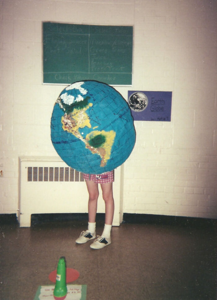 Child wearing a large earth globe costume with legs showing in a school hallway for funny school picture day fails.