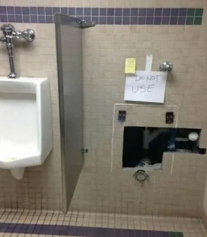 Bathroom wall with an open maintenance panel next to a urinal and a sign that made people laugh or do a double take.