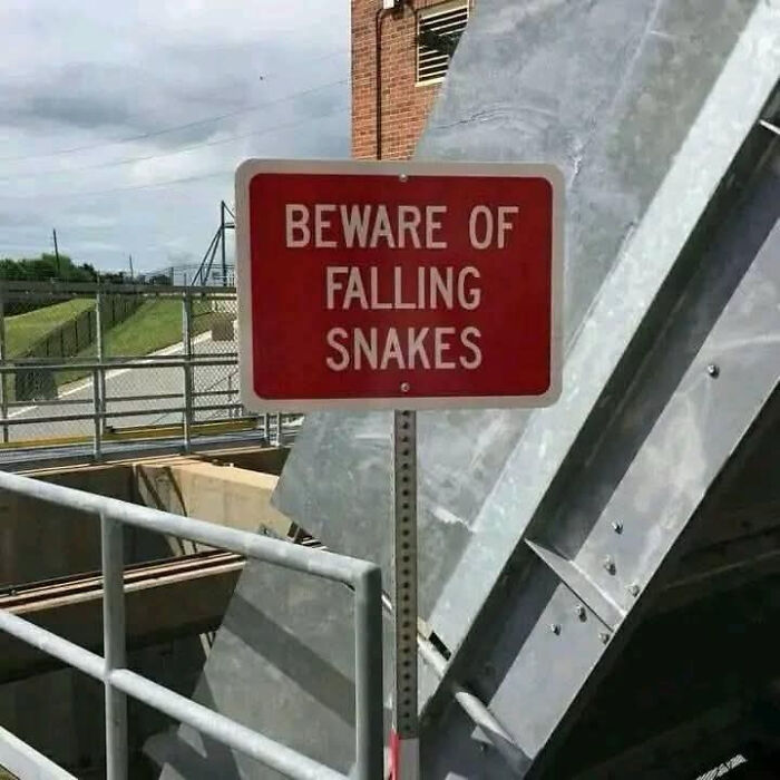 Red warning sign saying beware of falling snakes near industrial metal structures, a funny unusual sign among 73 signs.