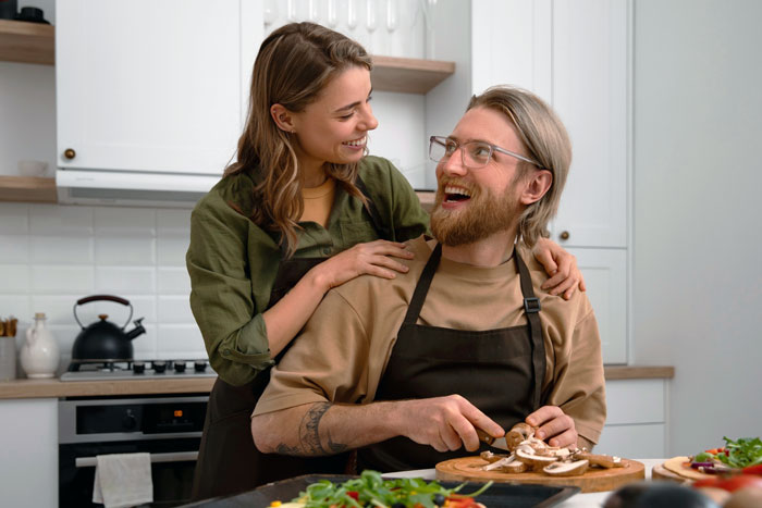 Smiling woman gives her boyfriend flowers in a kitchen, challenging sexist uncle's outdated views on gender roles.