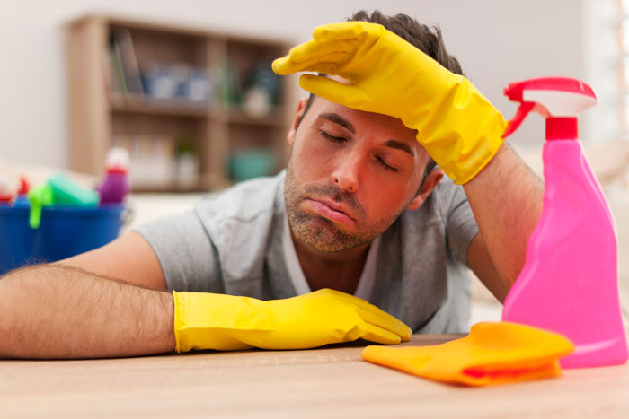 Man wearing yellow gloves, looking frustrated while resting on table with cleaning spray and cloth, tired of household chores. Man wearing yellow gloves, looking frustrated while resting on table with cleaning spray and cloth, tired of household chores.