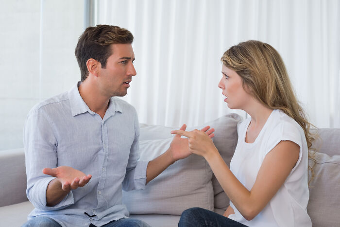 A man and woman arguing on a couch, illustrating a mansplaining conversation with visible frustration.