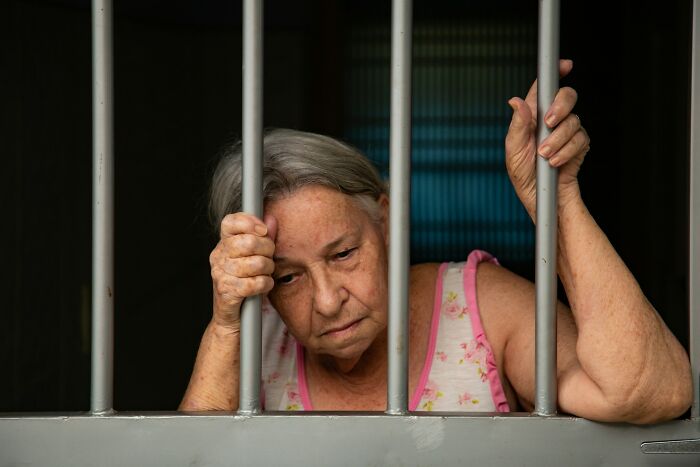 Elderly woman looking sad behind prison bars, illustrating moments people destroyed their own lives instantly.