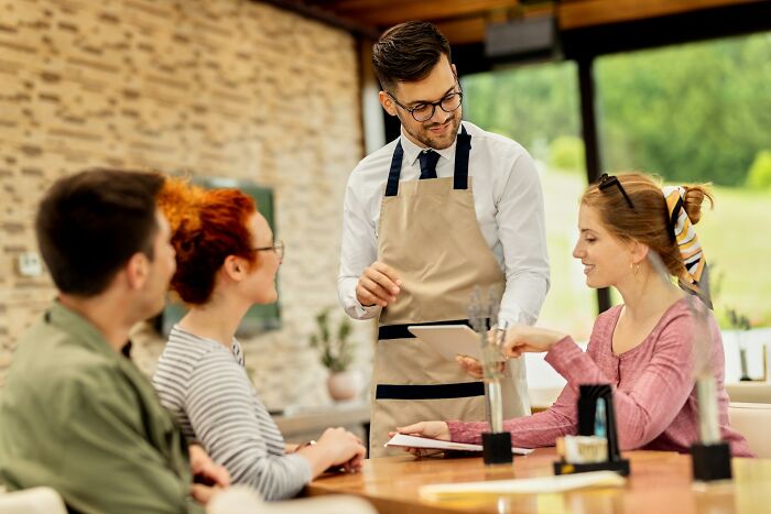Waiter in apron interacting with customers at a restaurant, illustrating hilarious and bizarre culture shock moments.
