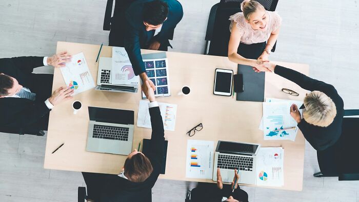 Business professionals shaking hands over a table with laptops and charts, representing shaky industries and trust issues.