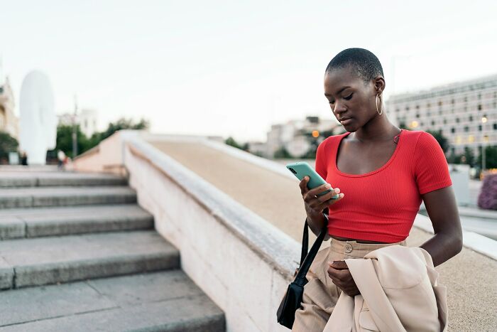 Young woman in a red top holding a phone outdoors, illustrating amazing women shutting down men’s creepy advances.