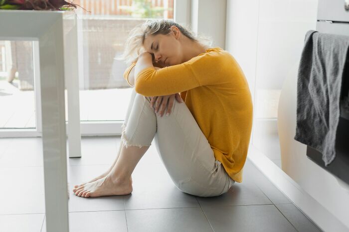 Woman in a yellow sweater sitting on the floor, appearing upset while reflecting on forgiving a cheating spouse.