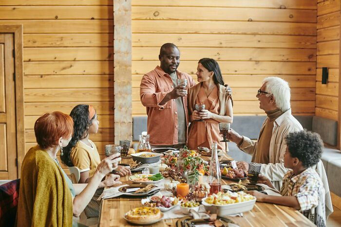 Family celebrating around a wooden table sharing drinks and food, showcasing weird and unhinged family traditions.