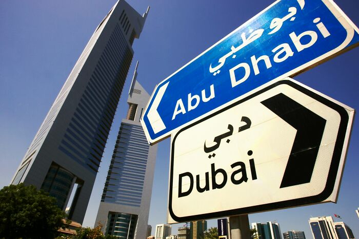 Street signs in Arabic and English for Abu Dhabi and Dubai with towering skyscrapers under a clear blue sky illustrating culture shock.