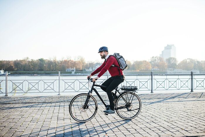 Man with helmet cycling by the river on a clear day, illustrating an active lifestyle with premium-tier zombie awareness.
