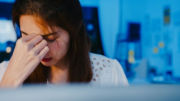 Young woman in a white top looking stressed and rubbing her forehead, illustrating regret and frustration with life hacks.