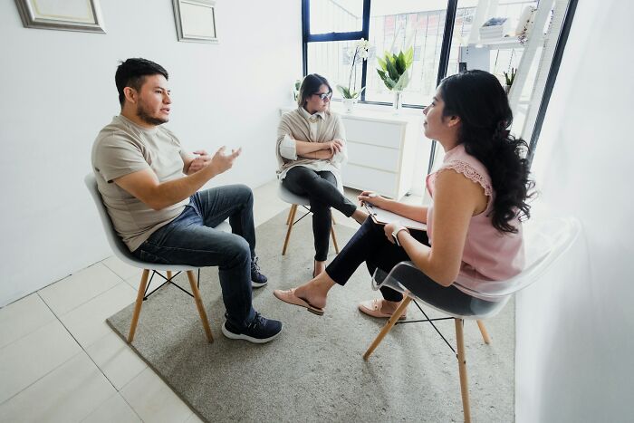 Couple discussing forgiveness with counselor in a bright room, exploring reasons to forgive a cheating spouse.
