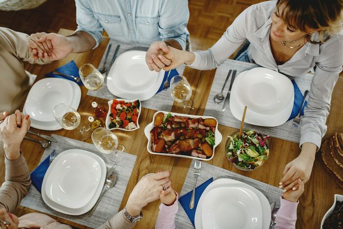 Family holding hands around a wooden table set with empty plates and dishes, highlighting unique family traditions.
