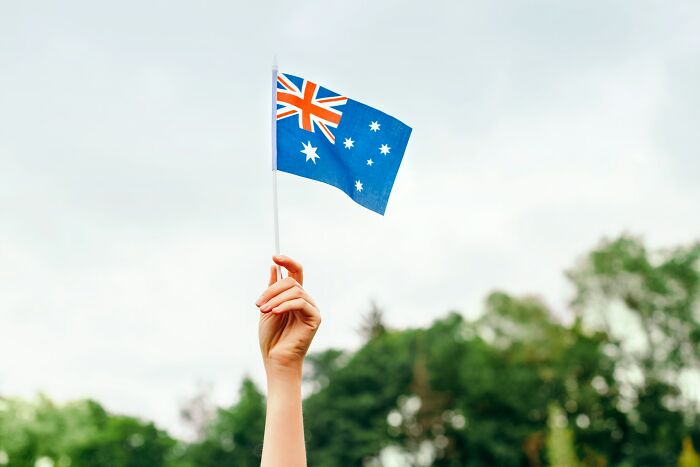 Hand holding Australian flag against sky, illustrating a hilarious and bizarre instance of culture shock for foreigners.