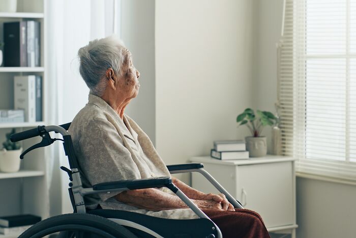 Elderly person in a wheelchair looking out a window in a quiet room, evoking stories of payback moments.