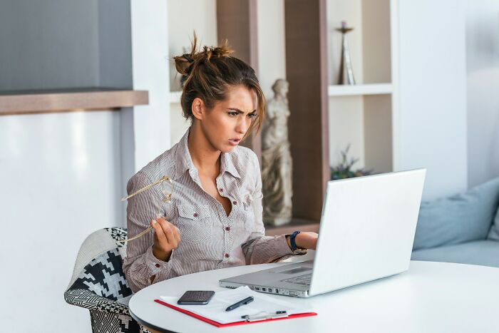 Woman looking confused at laptop screen, reacting to mystery and unexplained phenomenon while working from home.