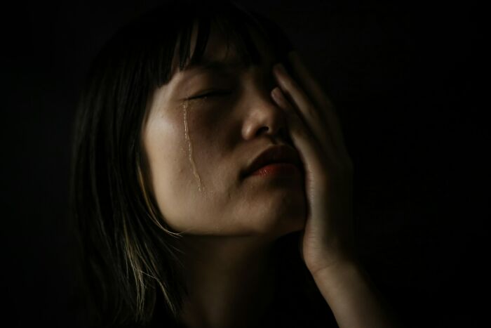 Person with tear on cheek and hand on face in dark setting, reflecting moments of payback that feel almost wrong to enjoy