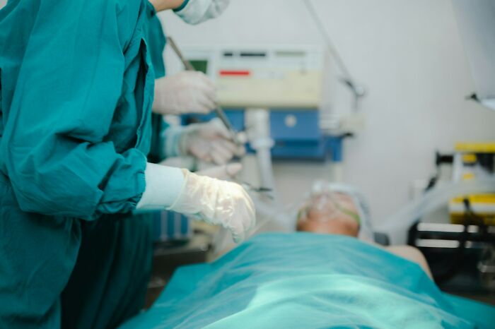 Surgeons in green scrubs performing a medical procedure on patient under anesthesia in an operating room setting.