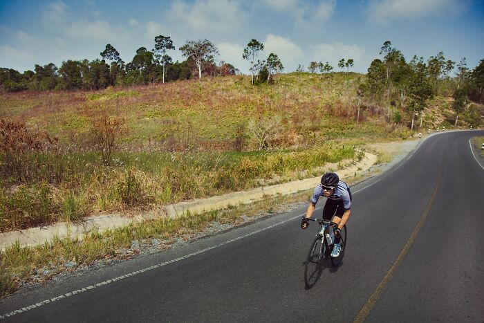 Cyclist riding fast on a winding road near a hillside, capturing one of the scariest experiences people still can’t believe.