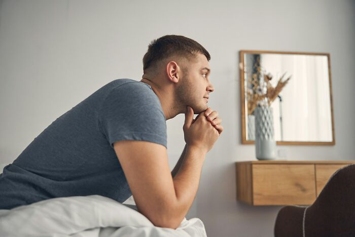 Young man in gray shirt looking thoughtful in a room, reflecting on bizarre encounters that left him questioning reality.