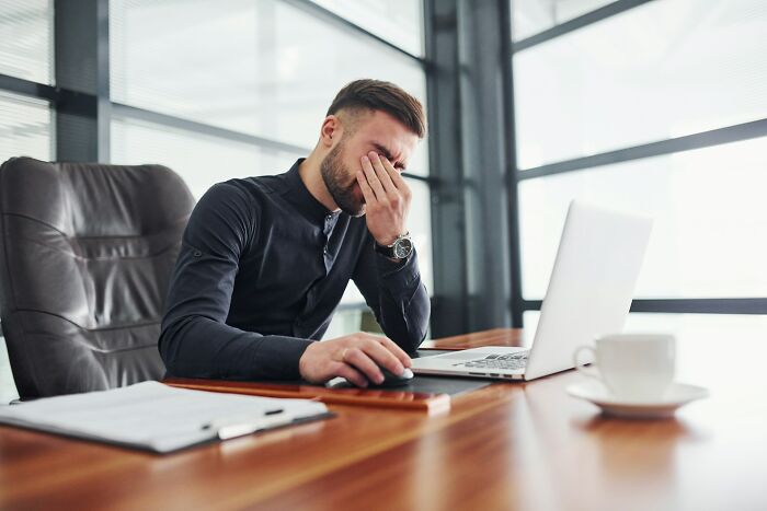 Man showing regret working on laptop at office desk, illustrating life hacks people regret ever trying concept