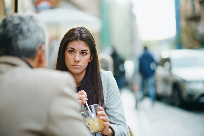 Young woman at outdoor cafe looking serious while shutting down man’s creepy advances during conversation.