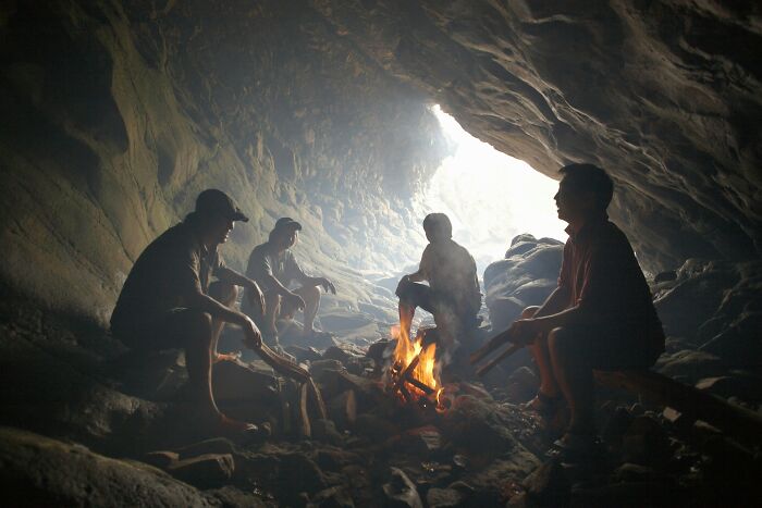 Four people sitting around a campfire inside a cave during a hiking trip in a remote wilderness area.
