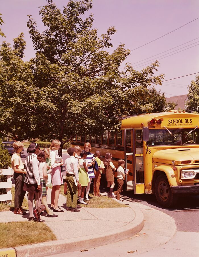 Children lining up to board a classic American yellow school bus, a real-life scene often seen in movies.
