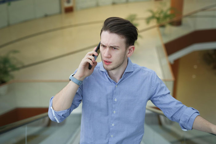 Young man on phone looking upset as he deals with relationship issues and his parents' reaction indoors on stairs.