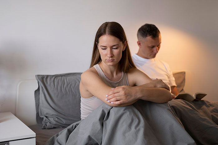 Couple sitting apart on bed looking upset, illustrating relationship struggles and fianc&eacute;e leaving in emotional moment.