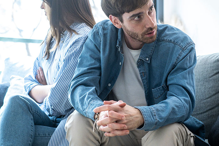 Man and fianc&eacute;e sitting apart on couch, looking upset and frustrated during a tense conversation about their relationship.
