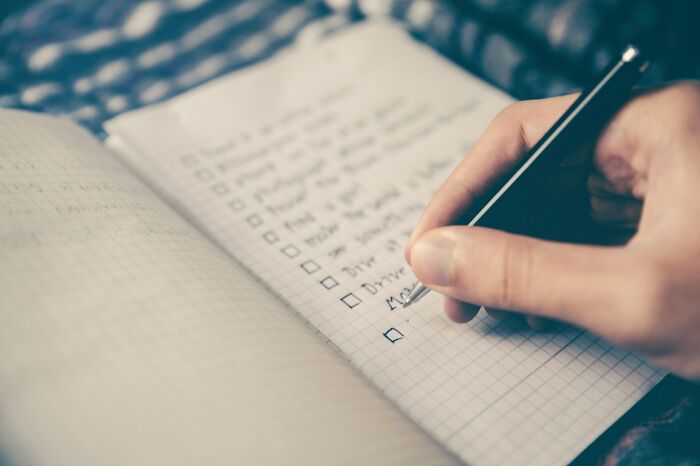 A person writing a checklist in a notebook, illustrating life hacks people regret ever trying.