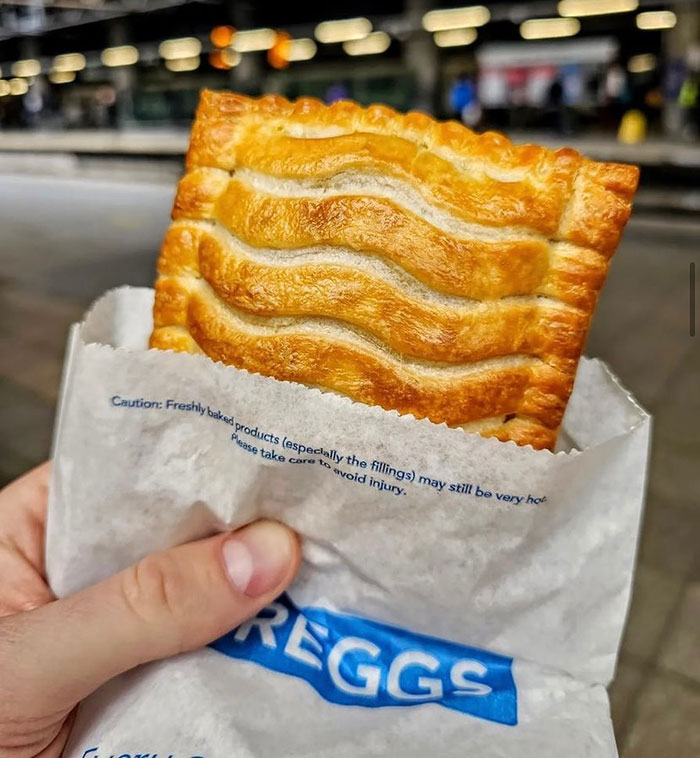 Hand holding a Greggs pastry in a paper bag with blurred urban background, related to King Henry VIII portrait time travel claim.