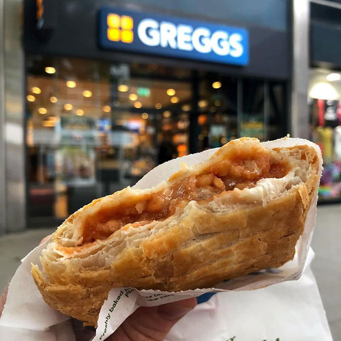 Hand holding a pastry outside a Greggs store, unrelated to King Henry VIII portrait or time travel claims.