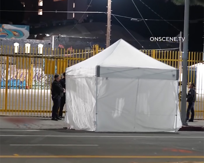 White forensic tent set up at a grisly scene in downtown LA with police officers securing the area at night.