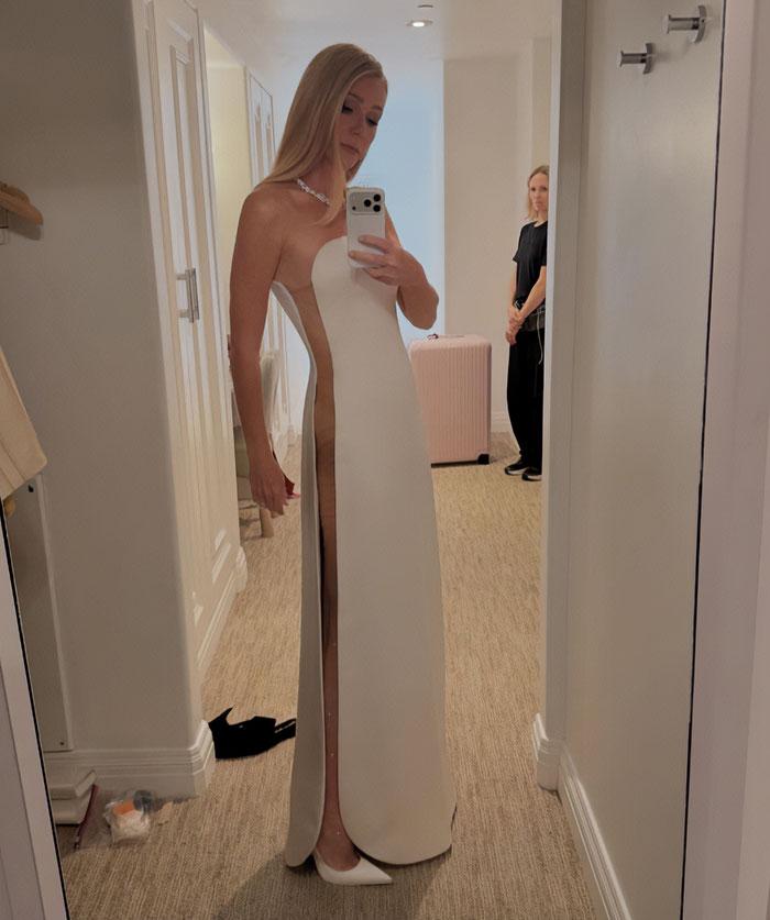 Gwyneth Paltrow wearing a sleek white racy Oscars dress backstage with aide standing awkwardly in the background.