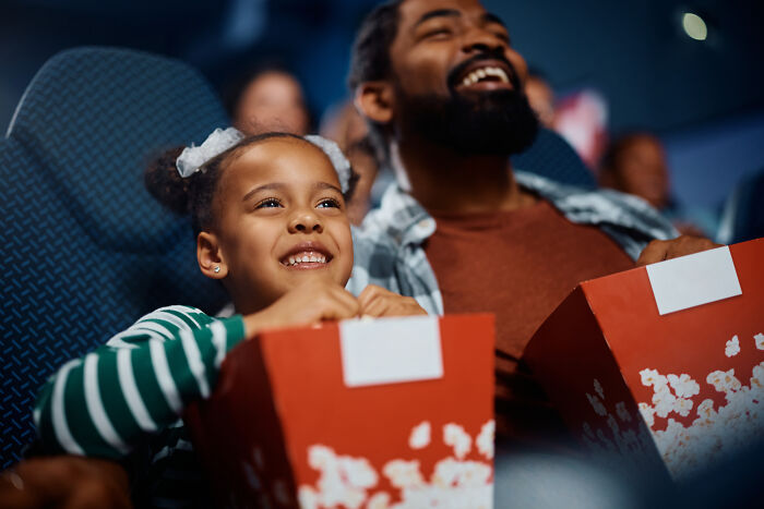 Father and daughter enjoying popcorn together in a movie theater, showcasing wholesome moments dads have with their kids.
