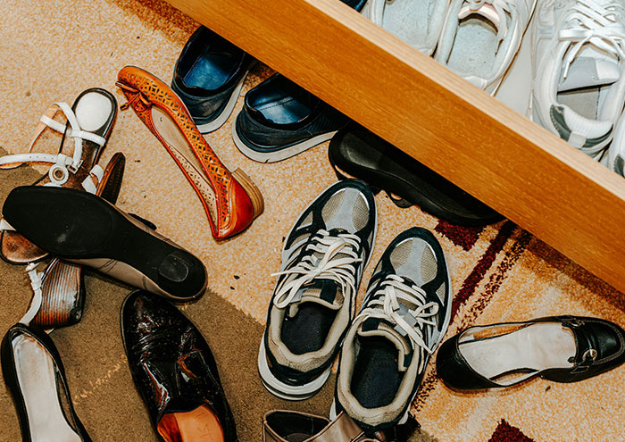 Various shoes scattered messily on the floor and inside an open wooden drawer, illustrating partners driving each other insane.