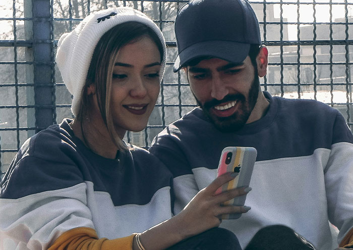 Couple sharing a fun moment while looking at a smartphone, illustrating seemingly harmless things partners do in relationships.