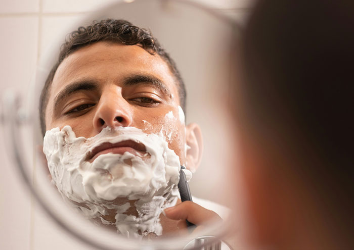 Man shaving with foam in front of the mirror, illustrating seemingly harmless things partners do that still drive people insane.